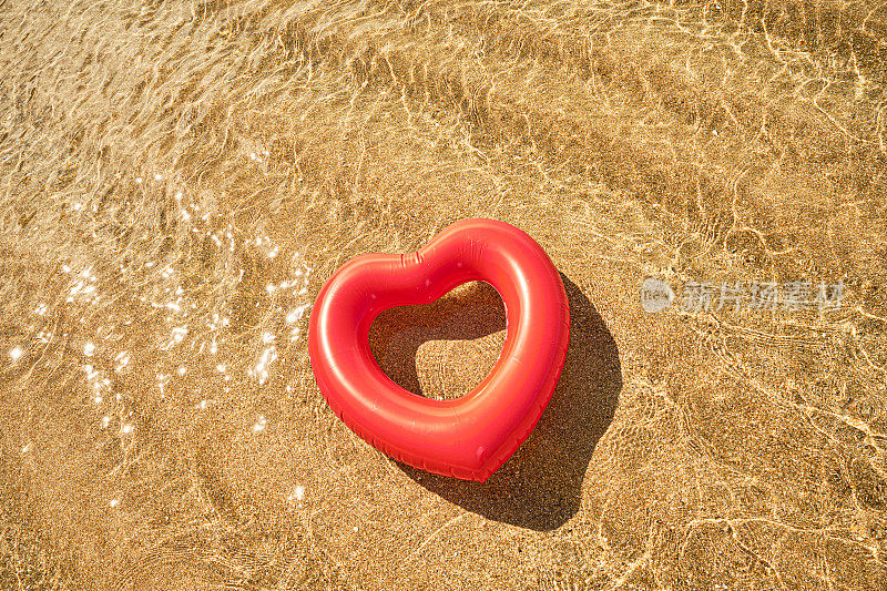 夏天的一天，康沃尔的Pedn Vounder海滩，红心形的橡胶圈漂浮在波光粼粼的浅海上。